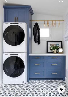 a washer and dryer in a laundry room with blue cabinets, white tile flooring and gold accents