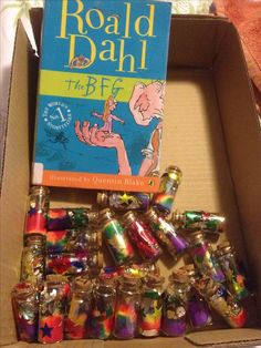 a box filled with lots of different colored glass jars next to a book on top of a table