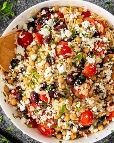 a white bowl filled with rice, beans and tomatoes next to a wooden spoon on top of a table