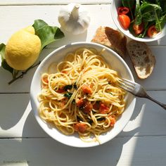 a white bowl filled with pasta next to a lemon and bread on top of a table