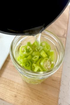 a glass jar filled with green peppers on top of a wooden cutting board