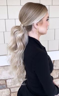 a woman with long blonde hair in a ponytail and black top is standing against a brick wall