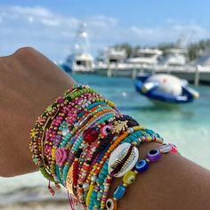 a person's arm with bracelets on it and boats in the water behind them