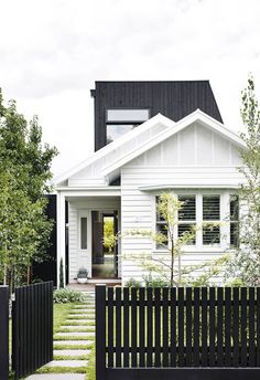 a white house with black fence and steps leading to the front door is surrounded by greenery