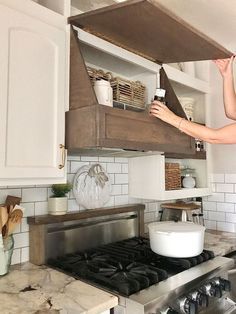 a woman is standing in the kitchen with her hand on an oven hood and reaching for something