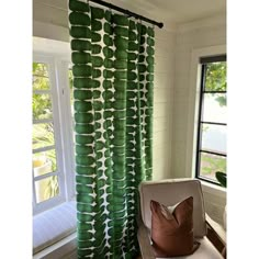 a green curtain hanging in front of a window next to a white chair with a brown pillow on it