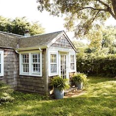 a small house with potted plants in front of it and trees around the yard