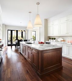 a large kitchen with wooden floors and white cabinets in the center, along with an island