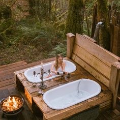 a woman sitting in an outdoor bathtub next to a fire pit