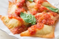 several pieces of ravioli with sauce and basil on a white plate, ready to be eaten