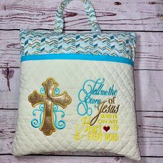 a white purse with blue trim and gold cross on the front is hanging from a wooden wall