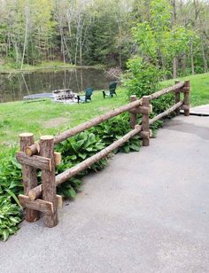 a fence made out of logs sitting in the middle of a park next to a lake