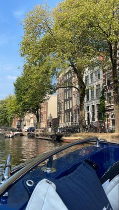 a boat traveling down a river next to tall buildings with trees on both sides and bicycles parked along the side