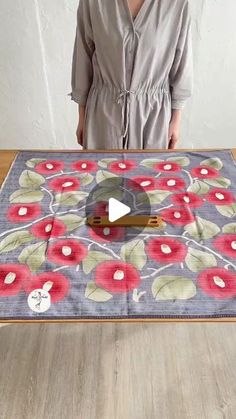 a woman is standing in front of a table with a flowered design on it