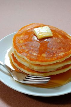 a stack of pancakes with butter and syrup on a plate next to a knife and fork