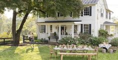 a woman standing in front of a white house next to a picnic table with food on it