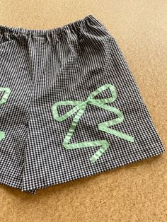 a pair of black and white checkered shorts with green letters on the side, sitting on a tan surface