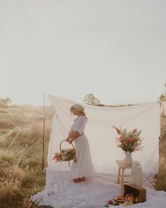 a woman in a white dress standing next to a table with flowers and fruit on it