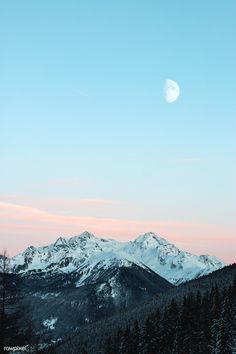 the moon is setting over some snowy mountains