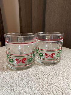 two glasses sitting on top of a white table next to each other with red and green bows