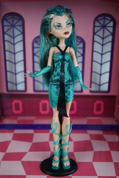 a doll with green hair and blue eyes standing on a checkered floor in front of a pink wall