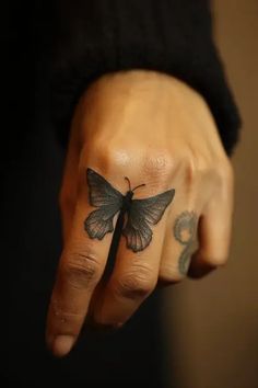 a person's hand with a small butterfly tattoo on their left thumb and finger