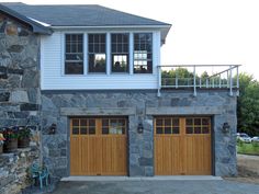 two garage doors are open in front of a house with stone walls and stairs leading up to the second floor