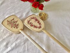 two decorative serving utensils sitting on a table with red roses in the background