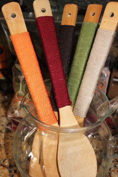 four wooden spoons in a glass bowl with different colored yarn wrapped around the handles