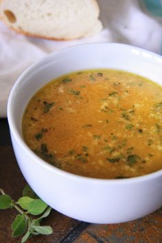 a white bowl filled with soup sitting on top of a table next to a piece of bread