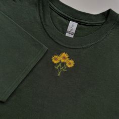 a green t - shirt with yellow flowers on the front and back, sitting on a white surface