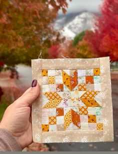 a person holding up a small piece of fabric in front of trees with fall foliage