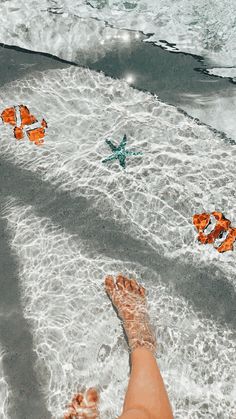 someone is laying down in the water with their feet on the beach and starfish