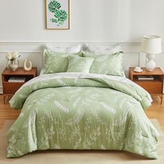 a bed with green and white comforters in a room next to a nightstand, lamp and painting