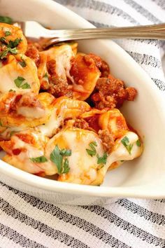 a white bowl filled with pasta and meat covered in sauce, parmesan cheese and herbs