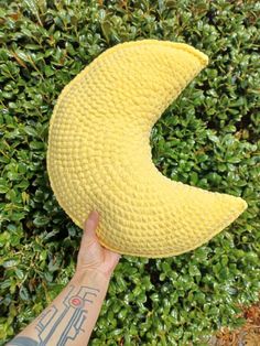 a person holding up a yellow banana cushion in front of some green bushes and shrubbery