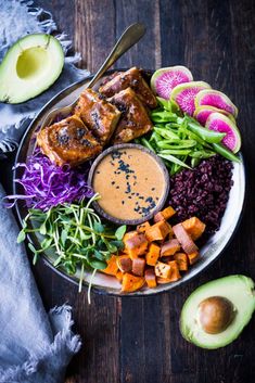 a plate filled with meat and vegetables next to an avocado