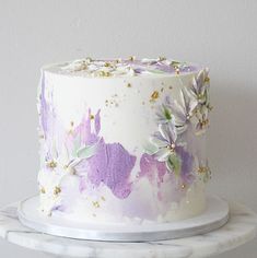 a white and purple cake with flowers on it sitting on top of a marble platter