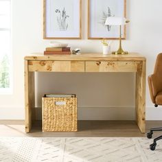 a wooden desk with two pictures on the wall and a basket underneath it next to a chair