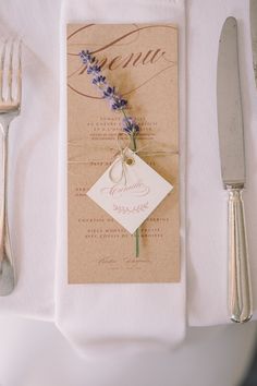 a place setting with silverware, napkins and flowers on the menu card for an elegant wedding