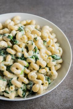 a white bowl filled with macaroni and cheese covered in spinach on top of a table