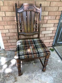 an old wooden chair sitting in front of a brick wall with a plaid seat cover on it