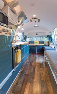 the interior of a camper van with wood floors and blue cabinets, stainless steel appliances