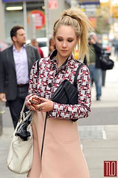 a woman walking down the street with a handbag in her other hand and looking at her cell phone