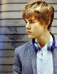 a young man with headphones standing in front of a wall wearing a suit and white shirt