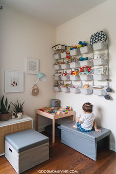 Child playing in a modern playroom with organized toy storage, featuring wall-mounted bins, a wooden table, and comfortable seating. The space is well-decorated with plants and artwork, creating a cozy and inviting atmosphere for children. Stylish Playroom, Children's Play Area, Play Corner