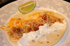 two tacos on a plate with sour cream, shredded cheese and lime wedges