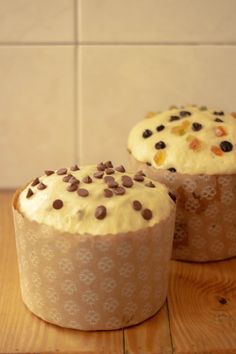 two cupcakes sitting on top of a wooden table covered in frosting and chocolate chips