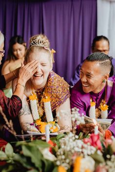 two women laugh as they sit at a table with candles in front of them and other people