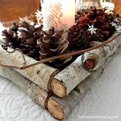 some pine cones and candles are in a wooden tray on a bed with white sheets